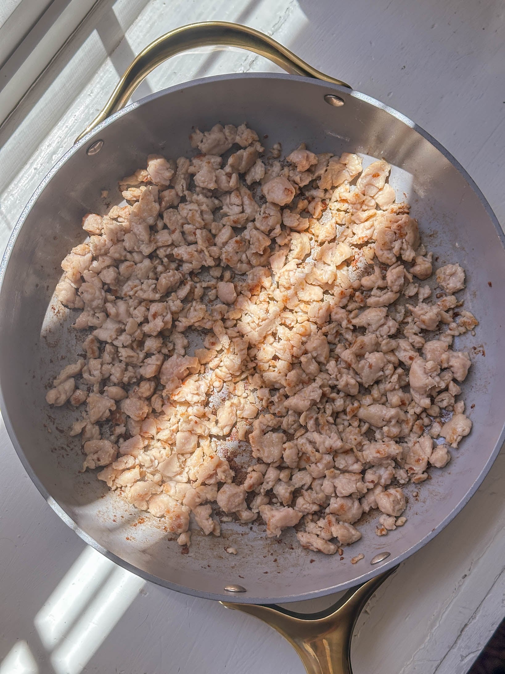 Cooked ground chicken in a pan with sunlight streaming through a nearby window.