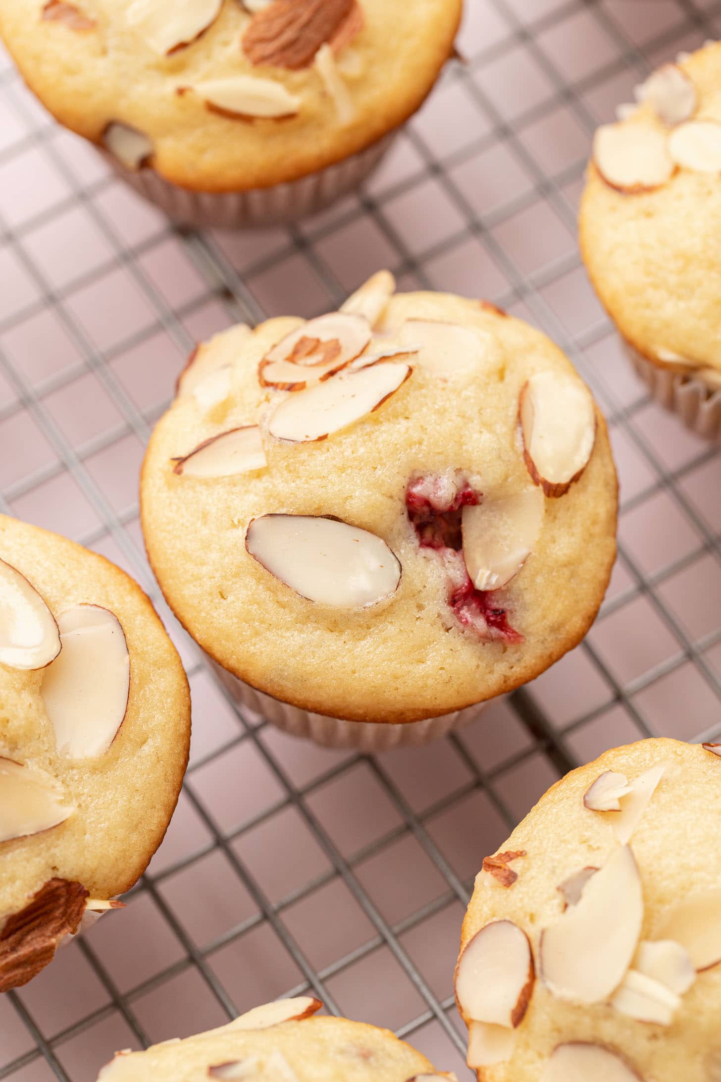 Almond muffins with berry filling on a cooling rack, topped with sliced almonds.