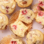 Almond muffins with raspberry centers, some sliced open, on a light background with scattered almond slices.