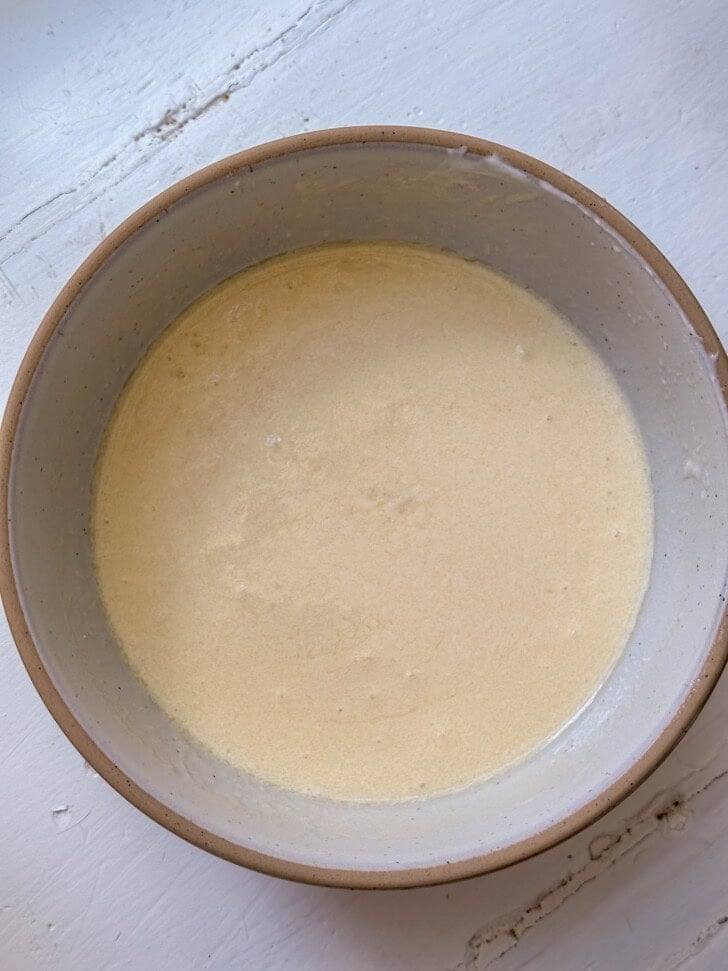 A bowl filled with pale, creamy batter sits on a white surface.