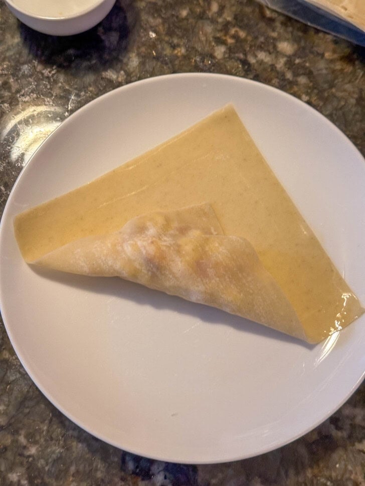 An eggroll is partially folded on a white plate atop a dark marbled countertop.