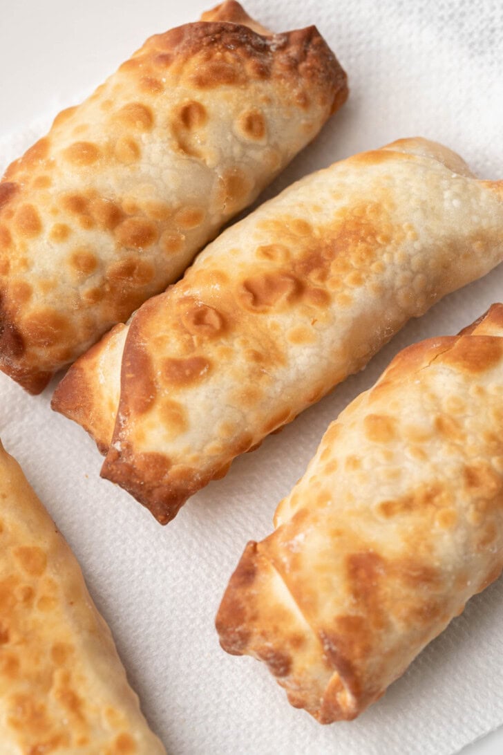 Three golden-brown egg rolls resting on a white paper towel, showing crispy, flaky texture.