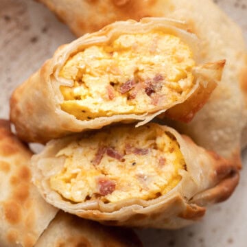 Closeup of crispy egg rolls cut open to show a filling of scrambled eggs and bacon on a plate.