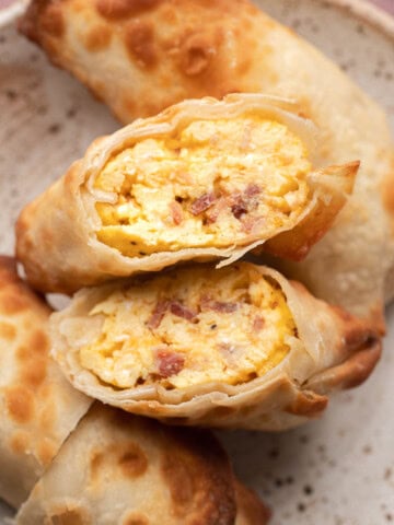 Closeup of crispy egg rolls cut open to show a filling of scrambled eggs and bacon on a plate.