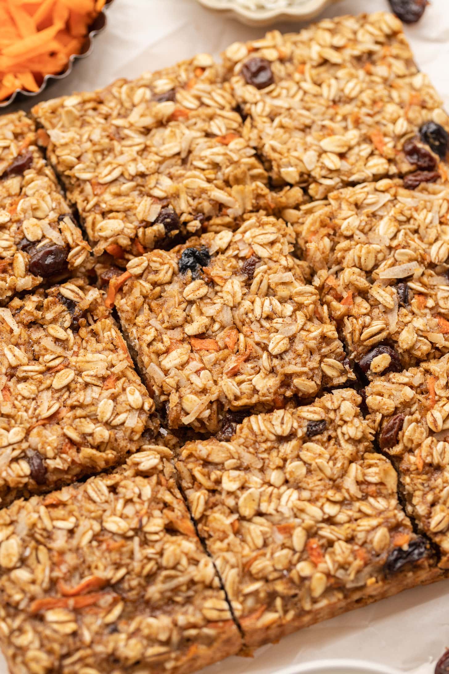 Close-up of baked oat bars with visible oats, raisins, and carrot shreds, cut into squares.