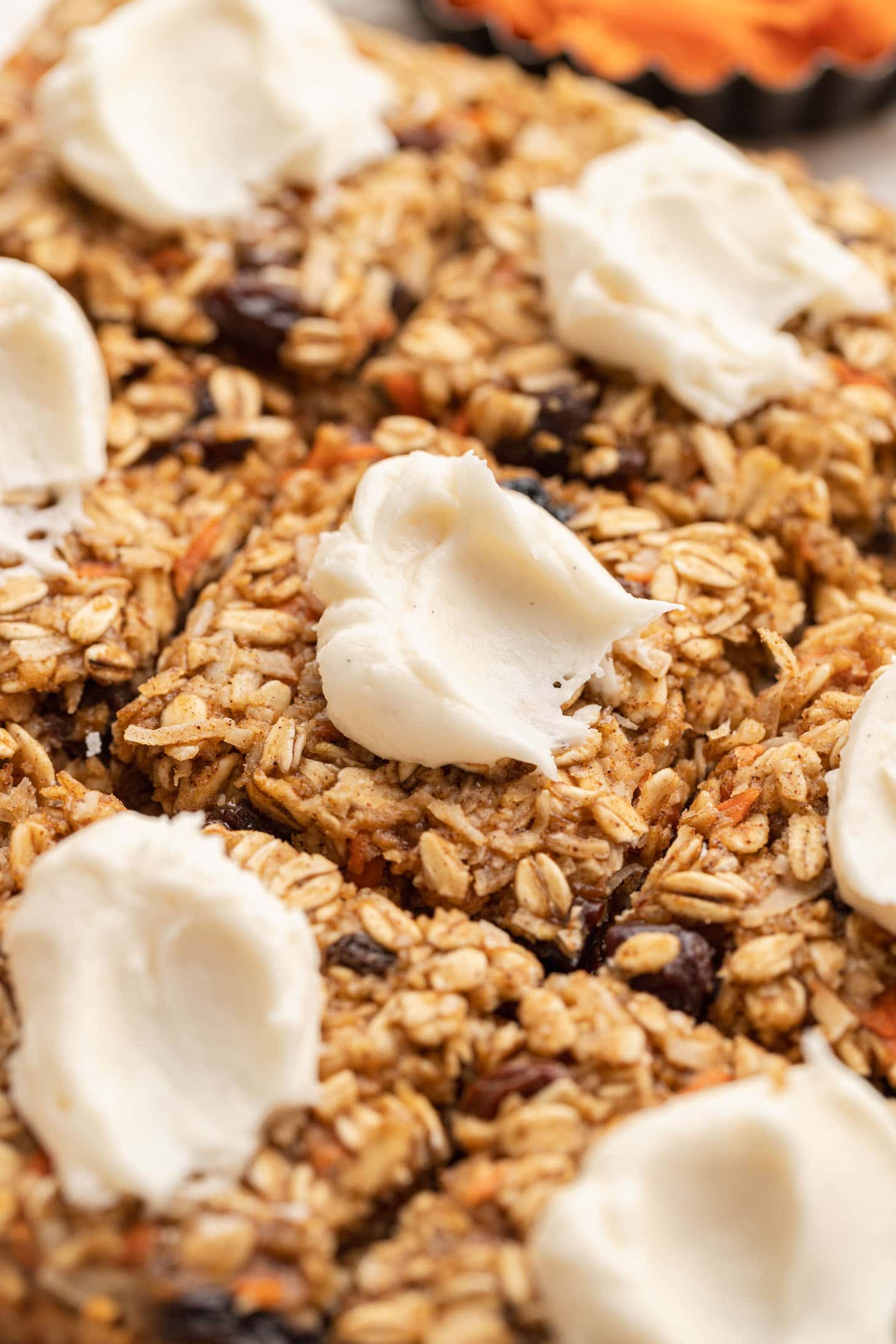 Close-up of oat bars topped with dollops of white frosting, showing texture and ingredients like oats and raisins.