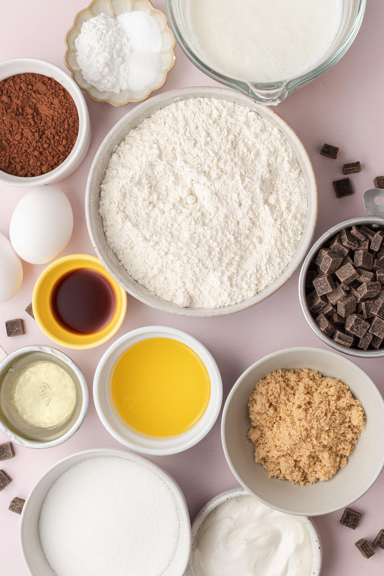 Baking ingredients in bowls, including flour, cocoa, sugar, eggs, butter, vanilla, chocolate, and milk.