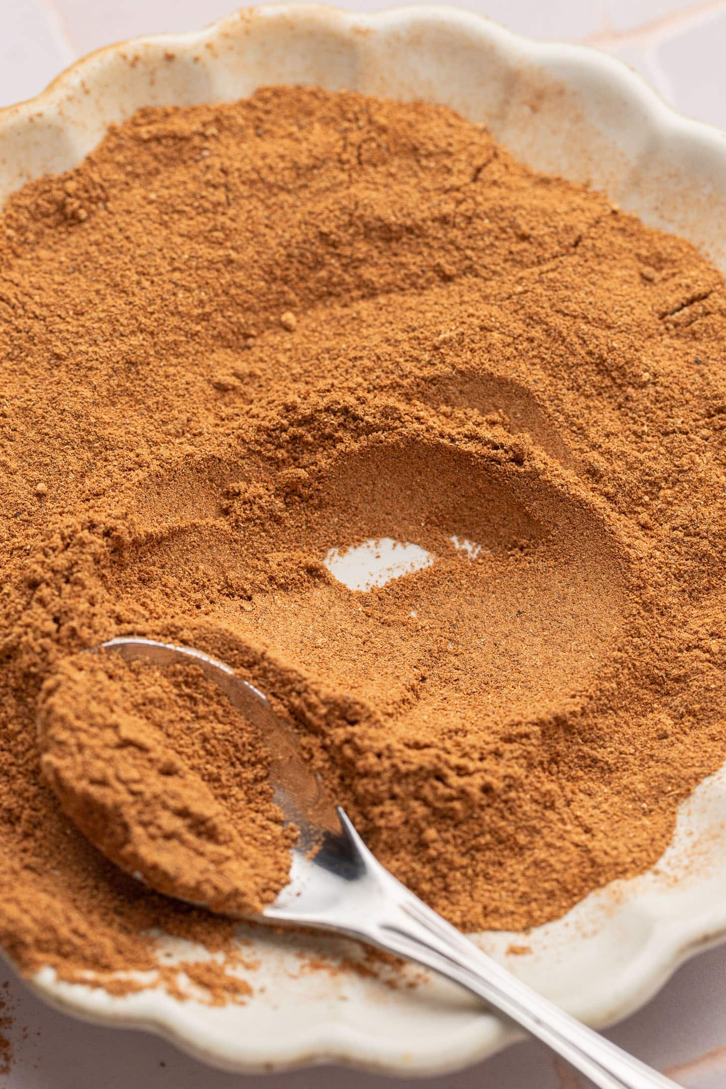 A spoon rests in a plate filled with a mound of ground cinnamon powder.