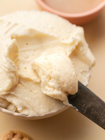 A knife spreads creamy butter in a bowl, with a honey dipper and a small dish in the background.