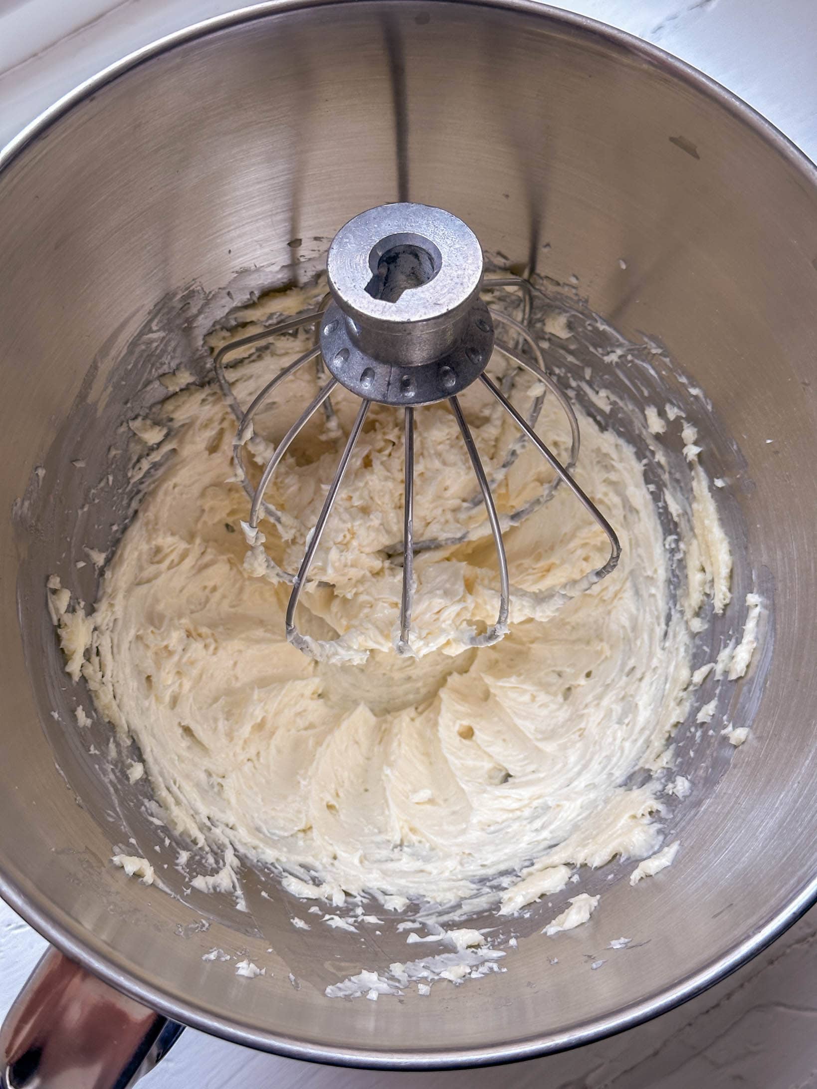 Creamy whipped mixture in a metal mixing bowl with a whisk attachment, viewed from above.