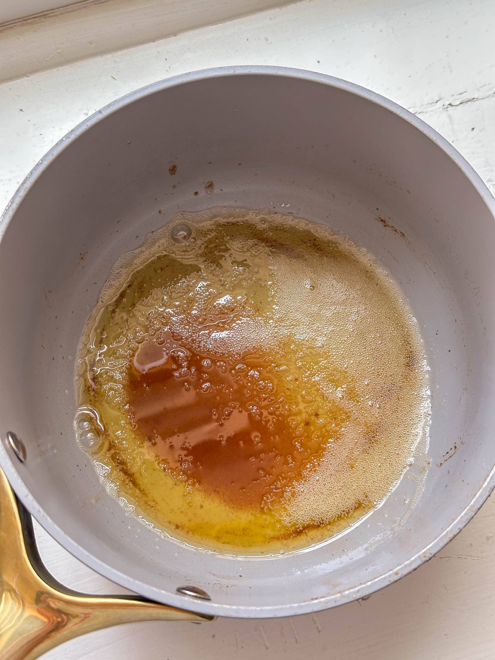 A saucepan with melted and browned butter sits on a white surface.