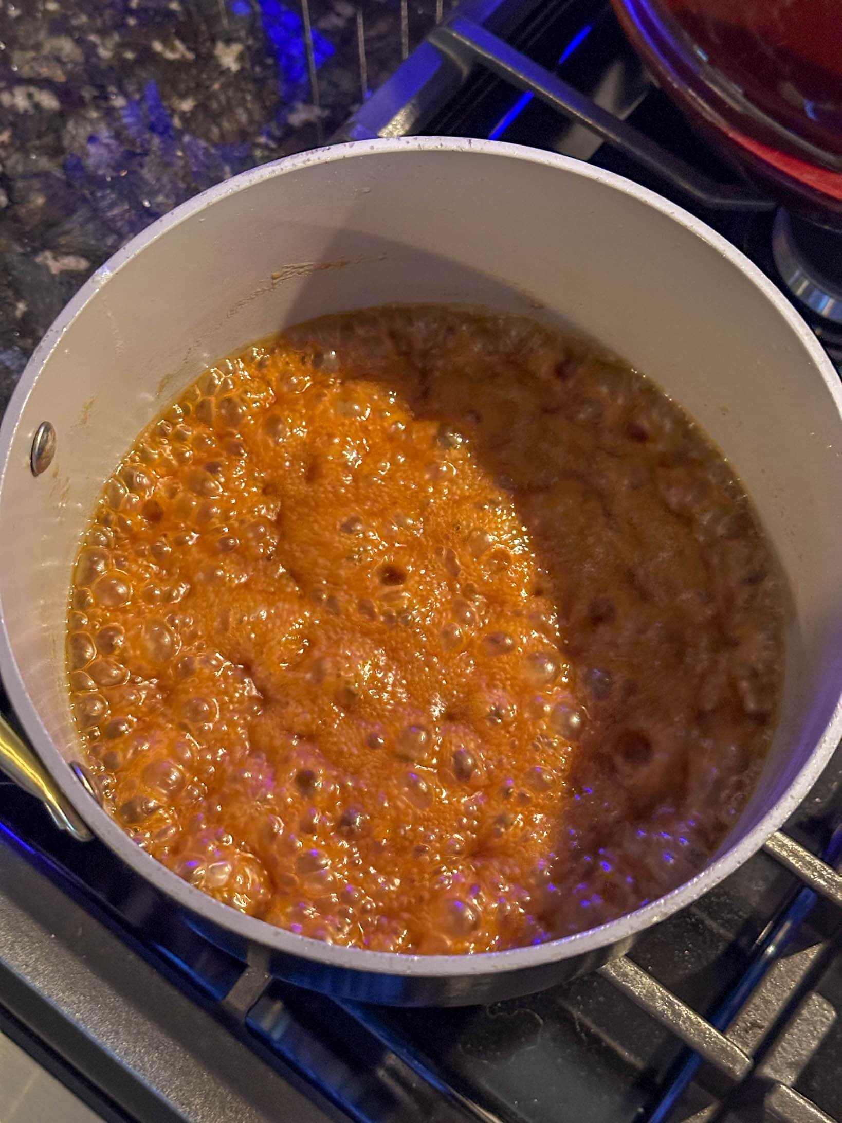 A pot of caramelizing sugar mixture bubbling on a stovetop, seen from above.