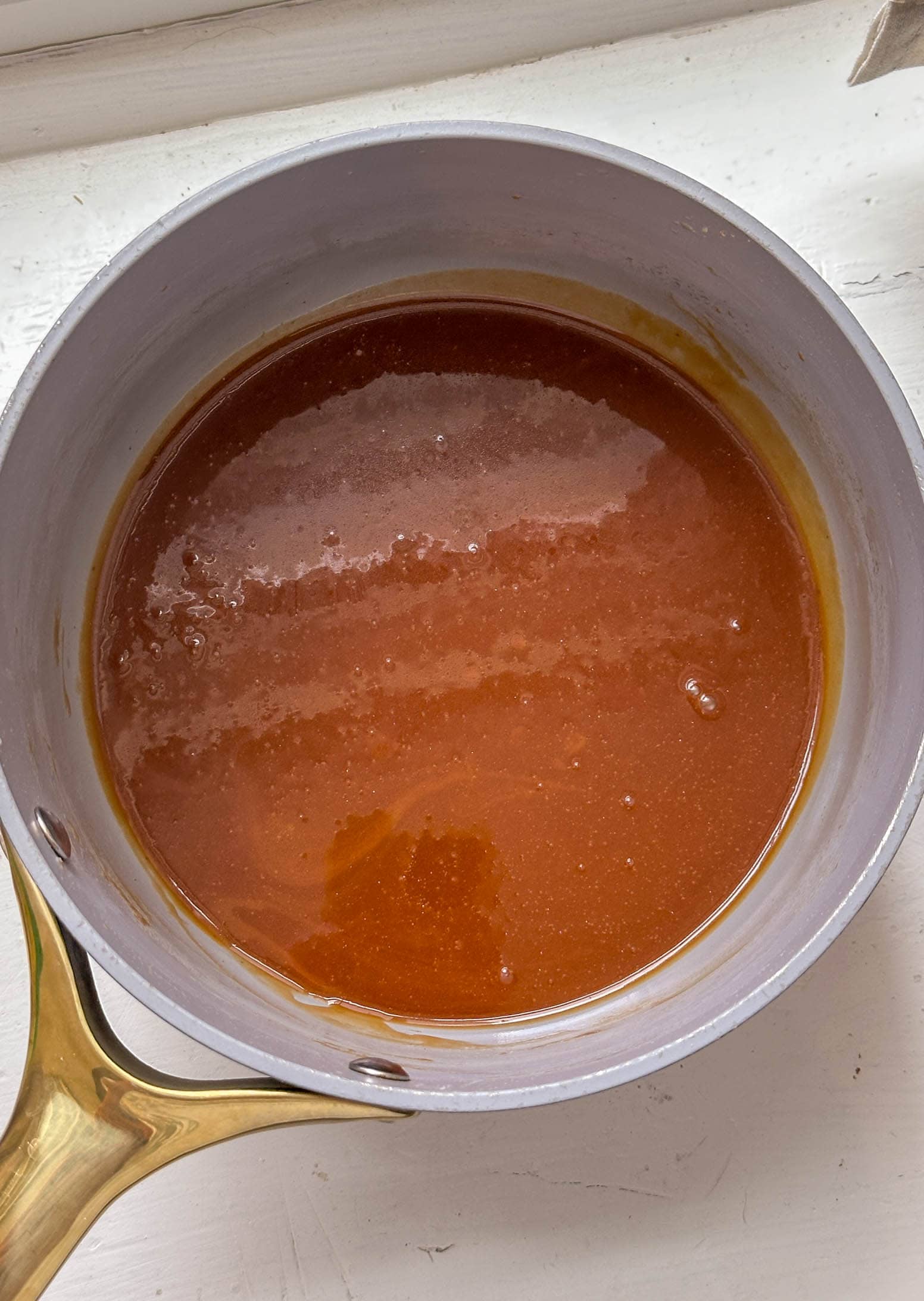 A saucepan filled with smooth, glossy caramel sauce on a white surface.