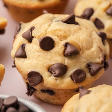Close-up of a chocolate chip muffin with chocolate chips scattered on top, surrounded by more muffins.
