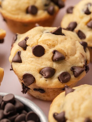 Close-up of a chocolate chip muffin with chocolate chips scattered on top, surrounded by more muffins.