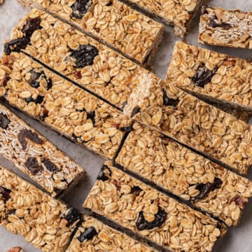 Homemade oat and dried fruit granola bars arranged on parchment paper, with pecans and dried fruit nearby.