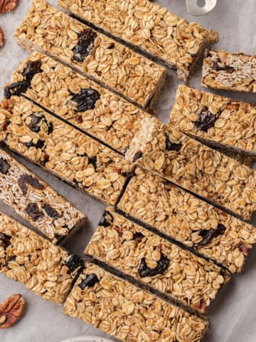 Homemade oat and dried fruit granola bars arranged on parchment paper, with pecans and dried fruit nearby.