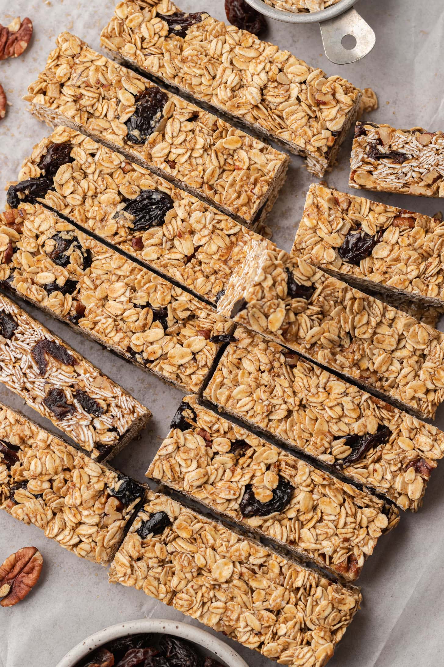 Homemade oat and dried fruit granola bars arranged on parchment paper, with pecans and dried fruit nearby.